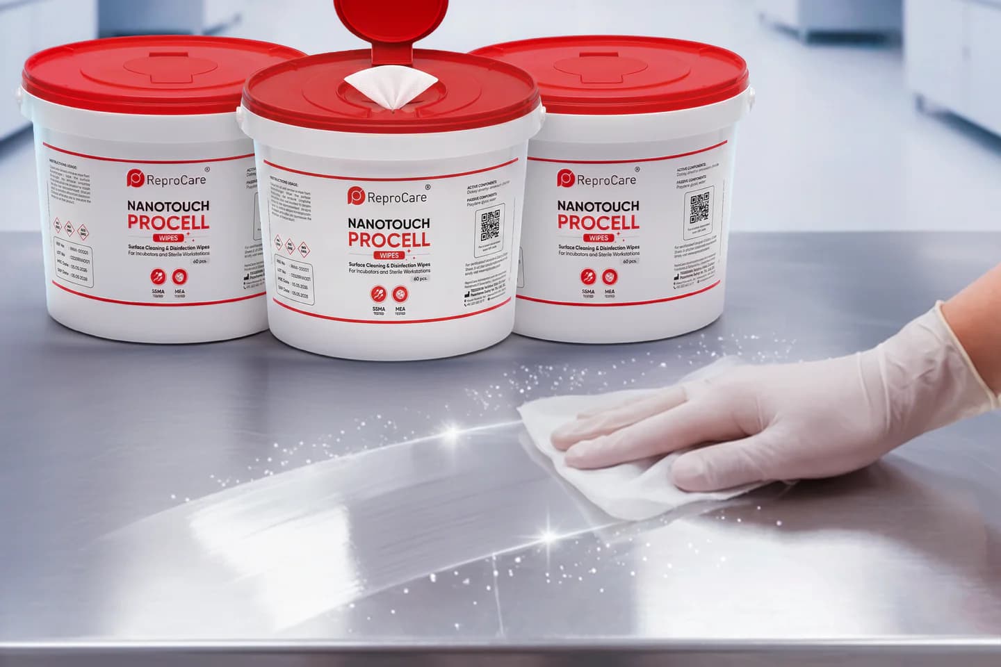 A gloved hand wipes a steel workbench in front of Procell Wipes tubs